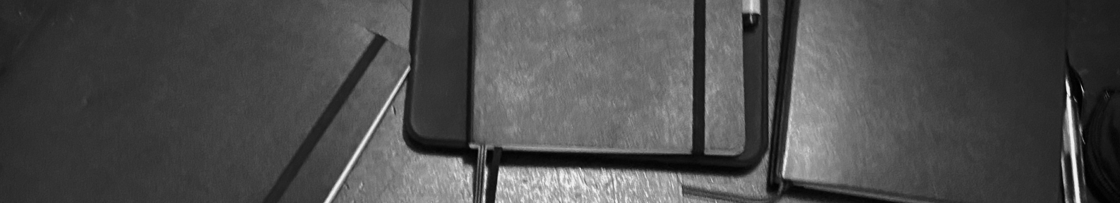 Three notebooks lie on a desk in a black and white image.
